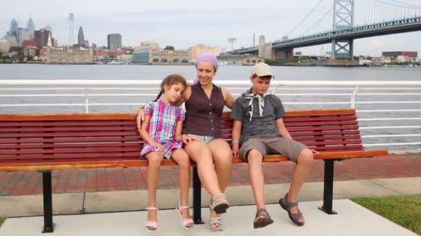 フィラデルフィアの背景にデラウェア州川堤防でベンチに座っている二人の子供を持つ母 — ストック動画