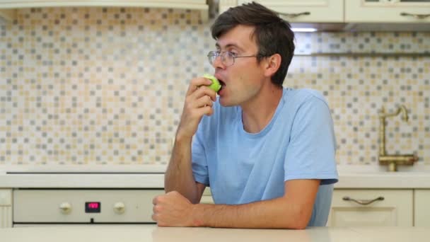 Hombre Con Gafas Camiseta Azul Comiendo Manzana Verde Mira Hacia — Vídeos de Stock