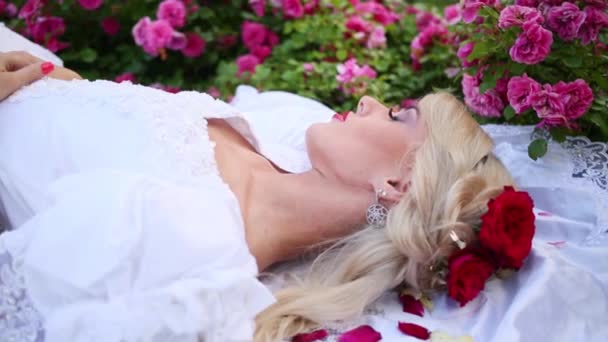 Γυναίκα Στην Λευκή Φόρεμα Ξαπλωμένη Στο Γρασίδι Ανάμεσα Παρτέρια Τριαντάφυλλα — Αρχείο Βίντεο