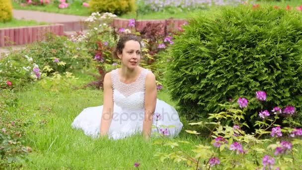 Vrouw Witte Jurk Zitten Gazon Tussen Bloemen Arborvitae Park — Stockvideo