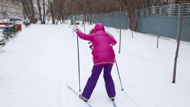 住宅建物近傍の積雪の中にピンクのスキーで女児裏 — ストック動画