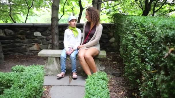 母と娘の話緑の夏の公園の石のベンチに座って — ストック動画
