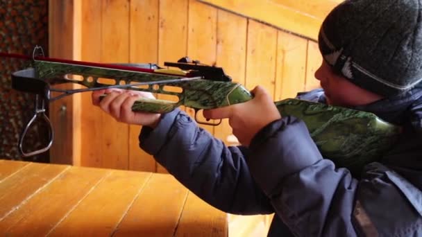 帽子で十代の少年が射撃でクロスボウを撮影します — ストック動画
