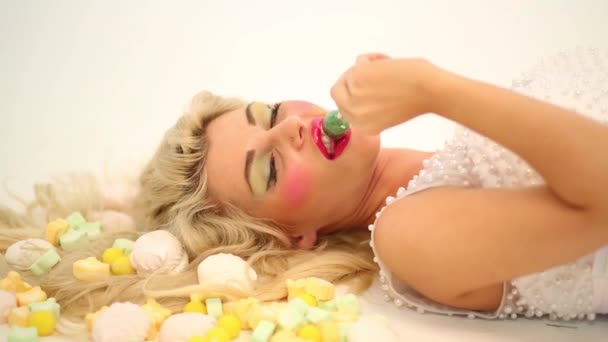 Lächelnde Frau Liegt Zwischen Süßigkeiten Und Saugt Lutscher Auf Dem — Stockvideo