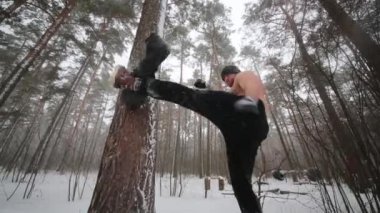 Çıplak göğüslü adam bacağını ile çam gövde bağlı eski kullanılan lastik başladı ve sonra sportsground kış ahşap üzerinde yumruk atıyor.