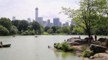 NYC, Amerika Birleşik Devletleri - 21 Ağustos 2014: tekneler oaring ve kayalık taş gölet New York Central Park içinde yakın oturan insanların dinlenme.