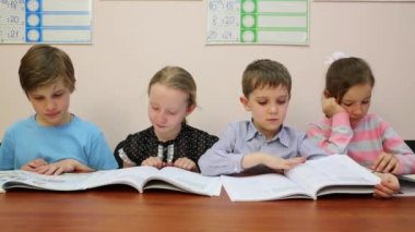 Dört çocuk bir kitap okuma bir masaya oturmak ve sayfaları çevir
