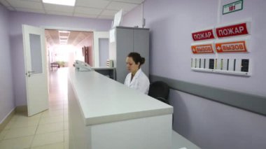 Bir kadın klinik bir masada oturur ve telefon cevaplar. Yazıtlar duvar - yangın ve arama