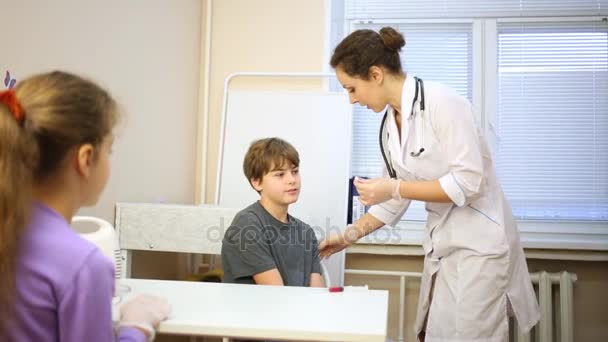 医療室で 人の子供が座っているし 女性医師が注入の少年の腕を準備 — ストック動画
