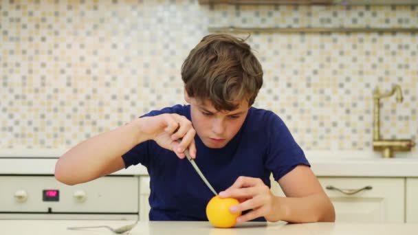 幸せな少年のティーンエイ ジャーはキッチン ナイフでオレンジをクリーンアップします — ストック動画