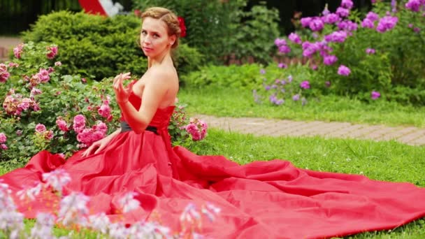 Rubia Vestido Rojo Con Falda Ancha Sentada Hierba Sosteniendo Brotes — Vídeos de Stock