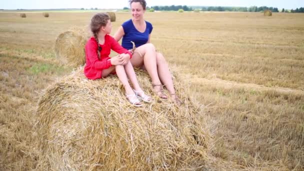 少女と母親は夏に刈ったフィールドに黄色のひるめし干し草の上に座る — ストック動画
