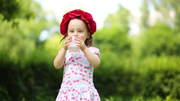 花の花輪でかわいい女の子が夏の公園で牛乳を飲みます — ストック動画
