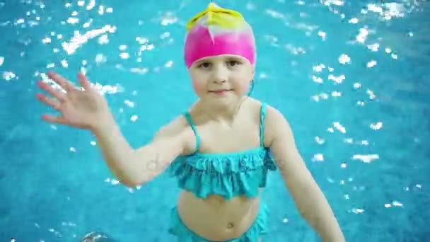 小女孩在游泳帽波浪手在蓝色水池 — 图库视频影像