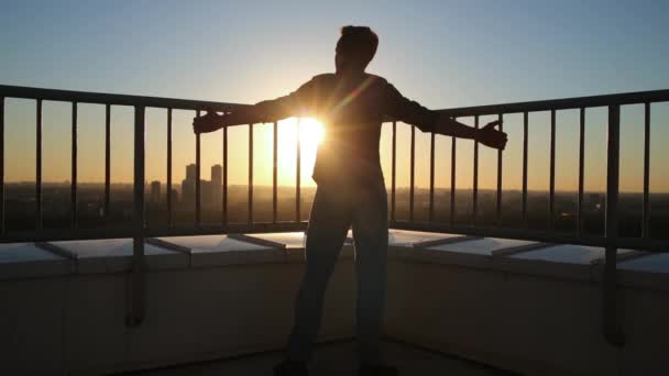 Man standing on roof of rail, hands spreading wide to side and looking at city and sunset. — Stock Footage Man Standing Roof Rail Hands Spreading Wide Side Looking City Royalty Free Stock Footage