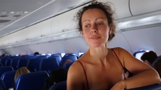 Smiling Woman Stands Airplane Cabin Leaning Seat Back — Stock Video