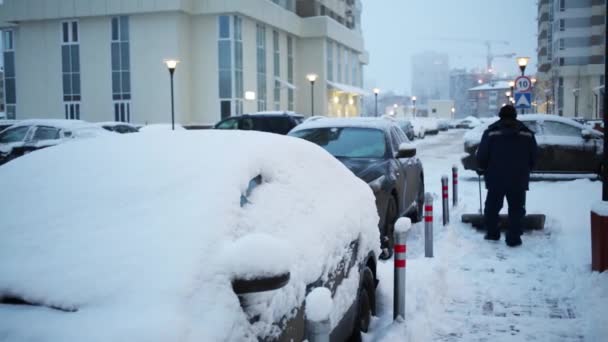 人的后面除雪在汽车停车场在冬天晚上附近住宅大厦 — 图库视频影像