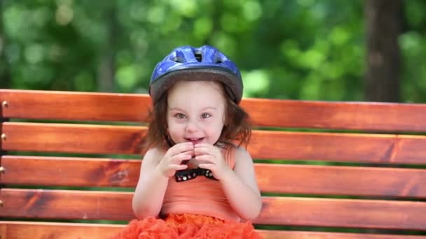 可爱的小女孩戴着蓝色头盔坐在板凳上的夏日 — 图库视频影像