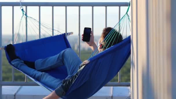 Młody Człowiek Leżący Niebieski Hamak Trzymając Smartfon Dyski Wokoło — Wideo stockowe