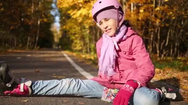 在秋天的森林里 一个穿着旱冰鞋和头盔的女孩坐在铁轨上 — 图库视频影像