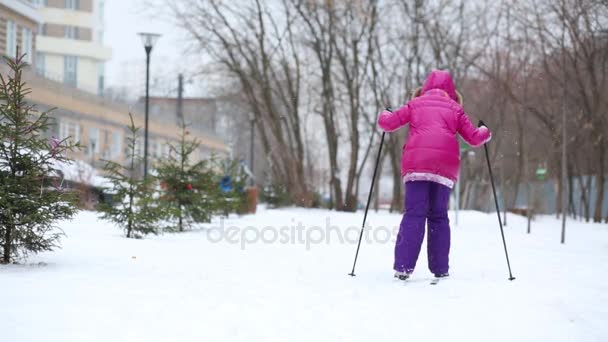 女の子子木の近くの雪の中にスキーと建物の裏 — ストック動画