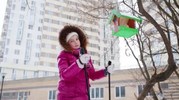 Barn Rosa Med Ski Poser Nära Träd Med Fågelbordet Snöfall — Stockvideo