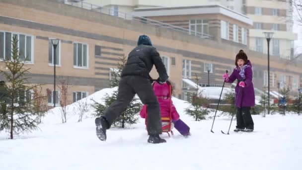 少年はピンクで女の子とそりをプッシュ 女の子はスキー 子供降雪中に歩く — ストック動画