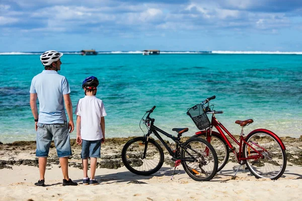 Far och barn på stranden med cyklar — Stockfoto