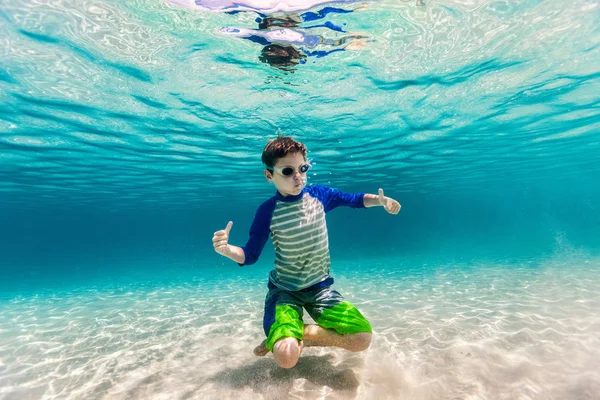 Cute teenage boy swimming underwater in shallow turquoise water at tropical beach