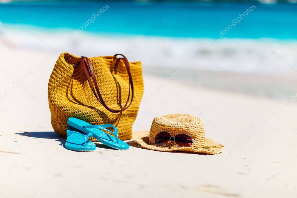 Straw hat, bag, sun glasses and flip flops on a tropical beach