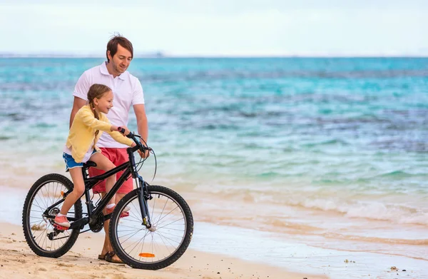 父亲教她骑自行车在海滩玩在一起的小女儿 — 图库照片