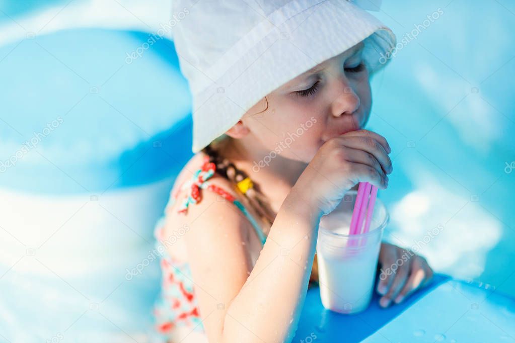 Cute little girl at all inclusive resort swimming pool sipping cocktail