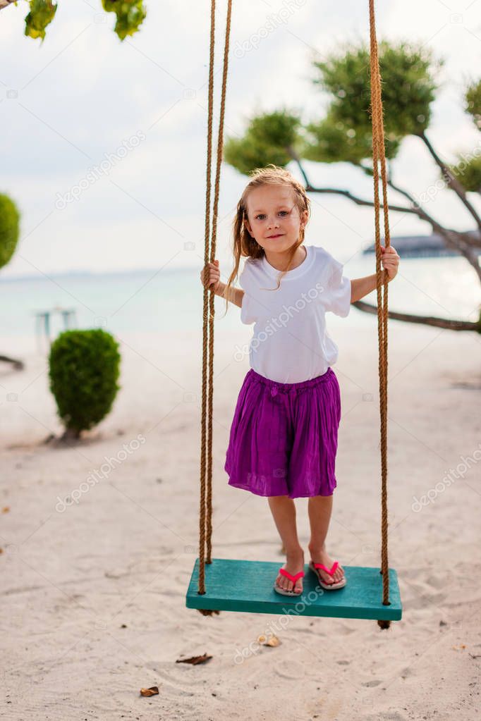 Adorable girl having fun swinging at tropical island beach