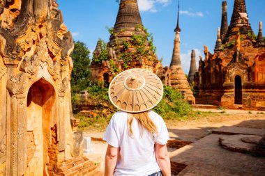 Back view of young woman visiting hundrets of centuries old stupas in Indein near lake Inle in Myanmar clipart