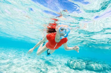 Tropikal okyanusta yüzen ve şnorkelle yüzen küçük bir kızın sualtı fotoğrafı.
