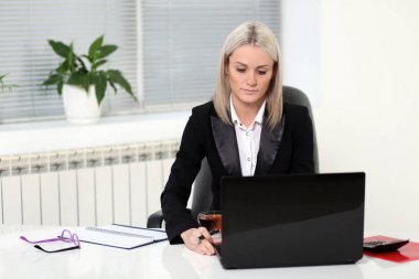 Dizüstü bilgisayar ve belgeler ile masada çalışan sarışın kadın