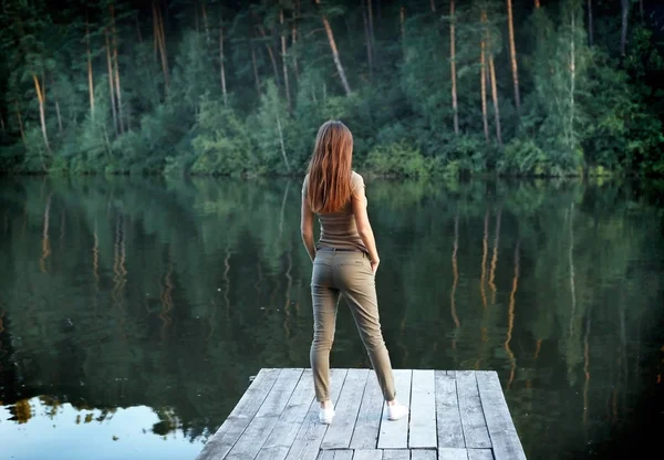 Menina de pé em um cais de madeira perto da água — Fotografia de Stock