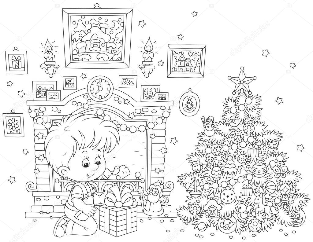 Little boy with his holiday gift near a fireplace and a colorfully decorated Christmas tree
