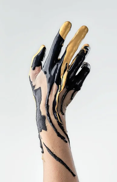 Vrouwelijke hand in vloeibare zwarte en gouden olie — Stockfoto