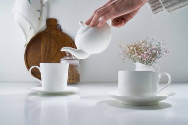 Açık gri arka planda beyaz porselen çay takımı ve narin bir buket çiçekle kompozisyon
