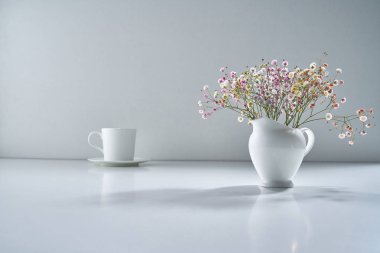 Açık gri arka planda beyaz porselen çay takımı ve narin bir buket çiçekle kompozisyon