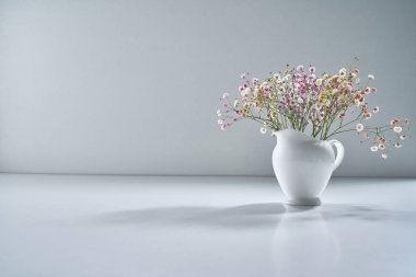 Açık gri arka planda beyaz porselen çay takımı ve narin bir buket çiçekle kompozisyon