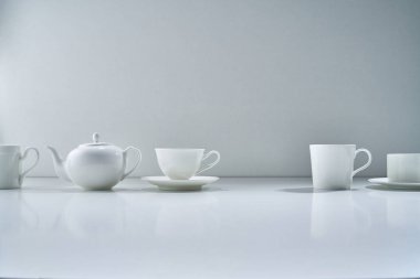 Açık gri arka planda beyaz porselen çay takımı ve narin bir buket çiçekle kompozisyon