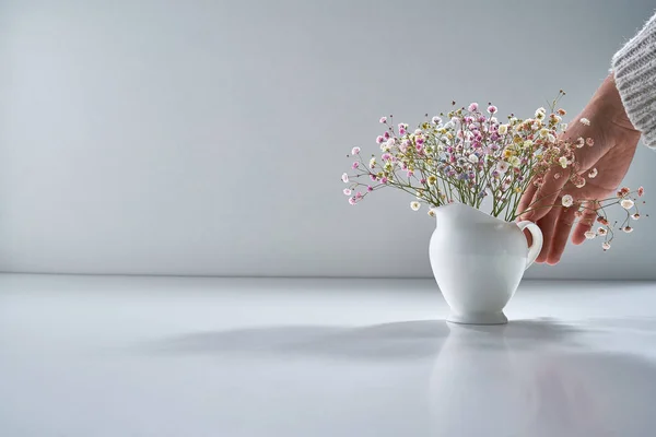 Composition with white porcelain tea-ware on a light gray background with a delicate bouquet of flowers