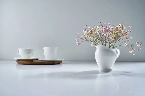 薄灰色の背景に白い磁器茶器と繊細な花束で構成されています — ストック写真