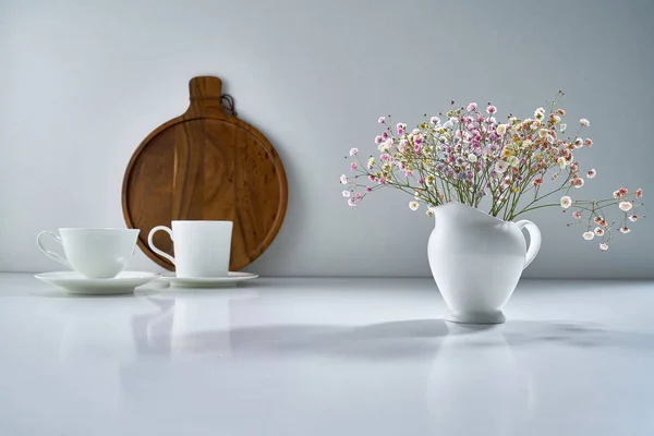 Composition with white porcelain tea-ware on a light gray background with a delicate bouquet of flowers