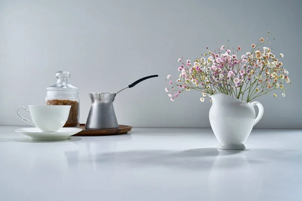 Composition with white porcelain tea-ware on a light gray background with a delicate bouquet of flowers