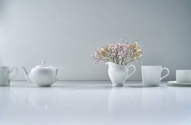 Açık gri arka planda beyaz porselen çay takımı ve narin bir buket çiçekle kompozisyon