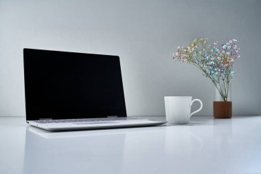 Modern bir dizüstü bilgisayar, beyaz bir fincan ve açık gri arka planda narin bir buket çiçekli diğer eski şeyler.