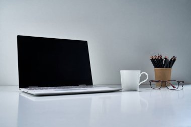 Modern bir dizüstü bilgisayar, beyaz bir fincan ve açık gri arka planda narin bir buket çiçekli diğer eski şeyler.